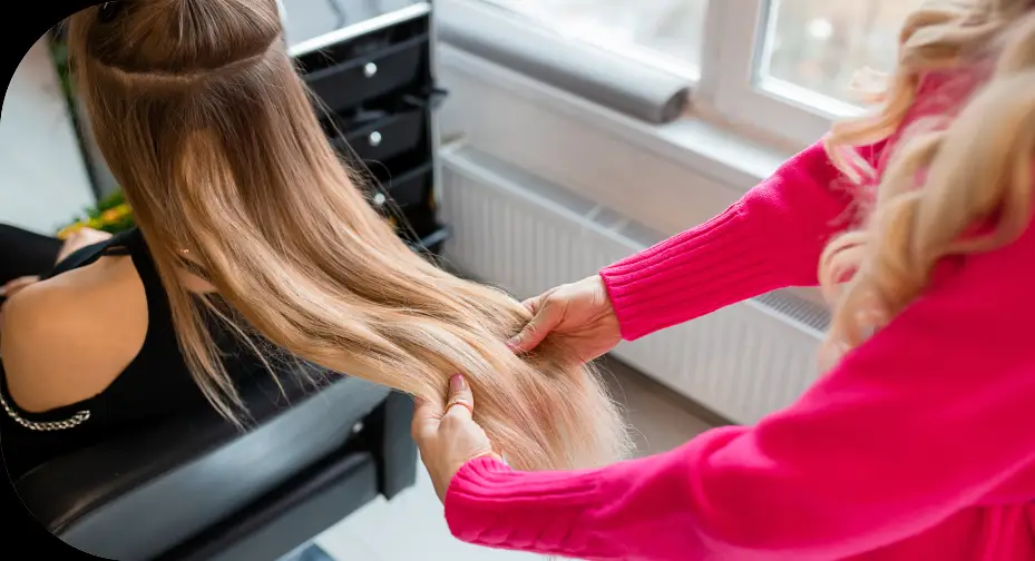 Stylist checking long blonde hair extensions on a client in a salon