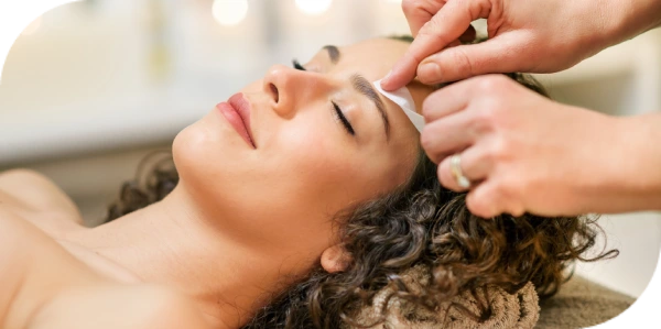 Esthetician performing eyebrow waxing on a relaxed client