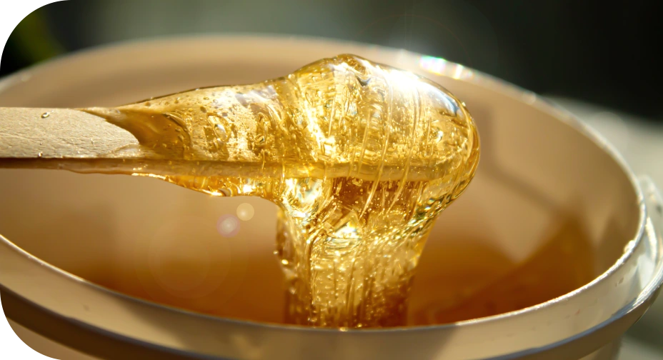 Close-up of warm golden wax on a wooden applicator for facial waxing