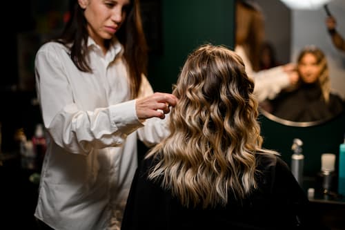 Professional hairstylist styling shoulder-length hair into soft waves at a salon