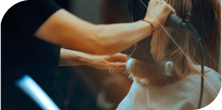 Stylist using a hair dryer and round brush to style a client’s hair