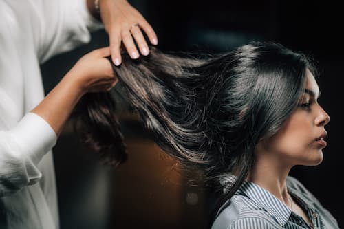Hairstylist lifting and styling long dark hair during a salon appointment