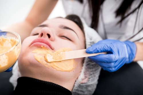 Esthetician applying facial mask to a client’s chin during skincare treatment