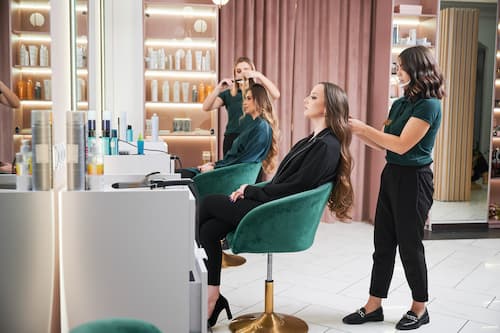 Hairdressers styling long hair for clients seated in salon chairs